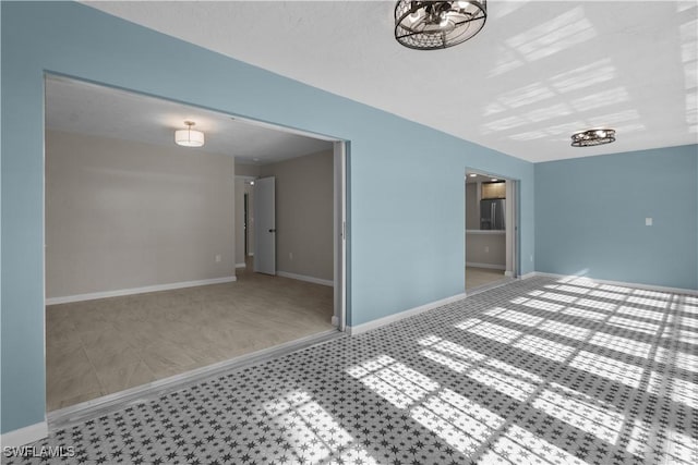 unfurnished room featuring baseboards and a notable chandelier