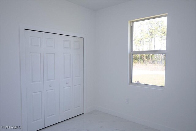 unfurnished bedroom with marble look tile flooring, baseboards, and a closet