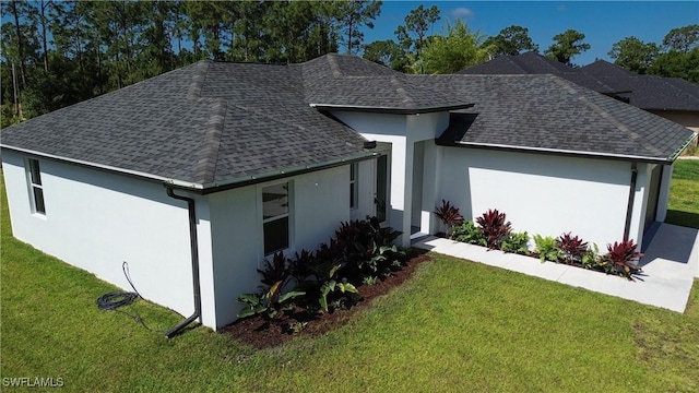 view of front facade featuring roof with shingles, stucco siding, and a front yard
