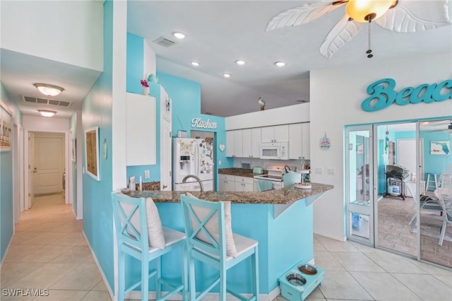 kitchen with white appliances, a breakfast bar area, light tile patterned floors, and ceiling fan