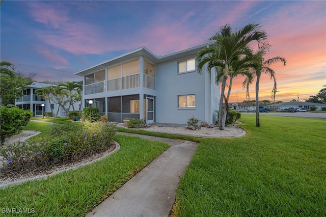 5032 Chiquita Blvd S Unit 101, Cape Coral, FL 33914 - back of house at dusk featuring stucco siding, a sunroom, and a lawn