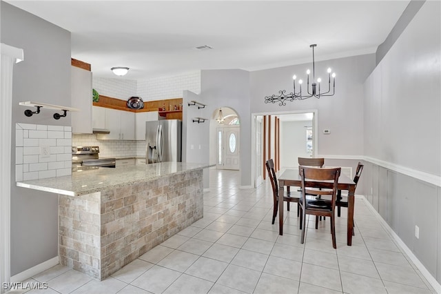 kitchen featuring light tile patterned floors, light stone countertops, a chandelier, appliances with stainless steel finishes, and backsplash