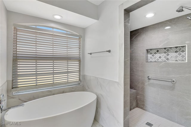 bathroom with a freestanding tub, plenty of natural light, tiled shower, and wainscoting