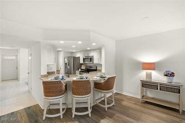 kitchen with light wood-type flooring, recessed lighting, white cabinets, light stone countertops, and appliances with stainless steel finishes