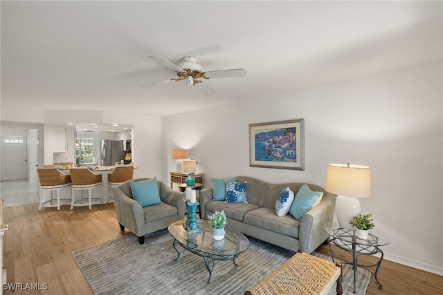 living room with light wood-type flooring, ceiling fan, and baseboards