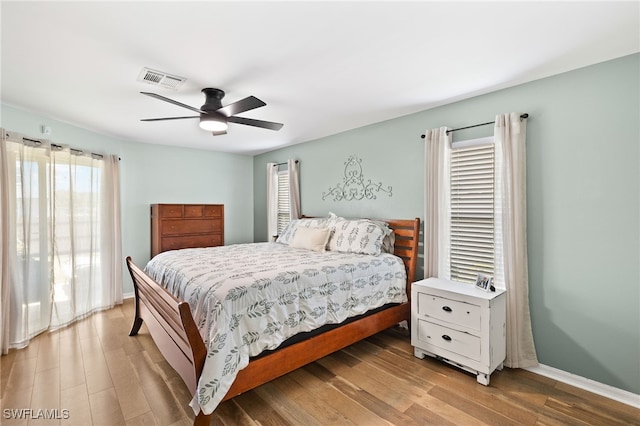 bedroom with baseboards, visible vents, a ceiling fan, and light wood finished floors