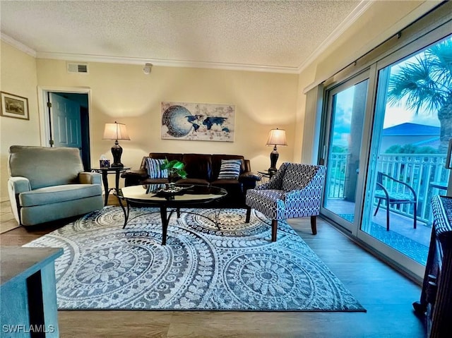living room with crown molding, a textured ceiling, visible vents, and wood finished floors