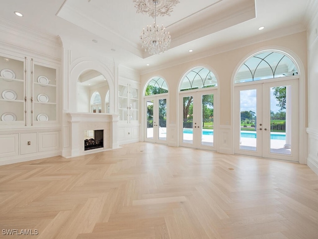 unfurnished living room with a notable chandelier, french doors, built in features, and a raised ceiling