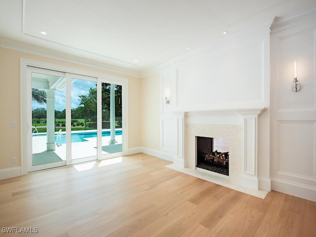 unfurnished living room featuring baseboards, a decorative wall, ornamental molding, a tiled fireplace, and light wood-style floors
