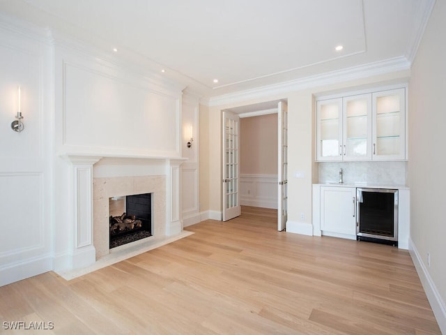unfurnished living room with a fireplace, a decorative wall, light wood finished floors, beverage cooler, and bar
