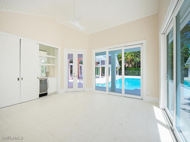 interior space with baseboards, vaulted ceiling, french doors, beverage cooler, and light floors