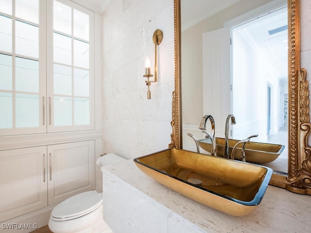 bathroom with a sink, tile walls, crown molding, and toilet