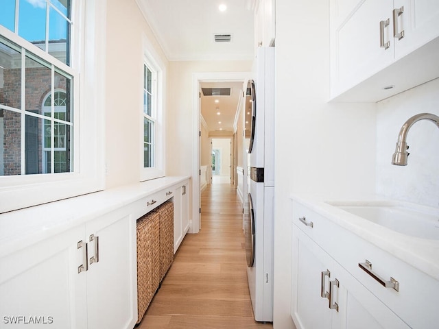 interior space with visible vents, a sink, ornamental molding, stacked washer / drying machine, and light wood finished floors