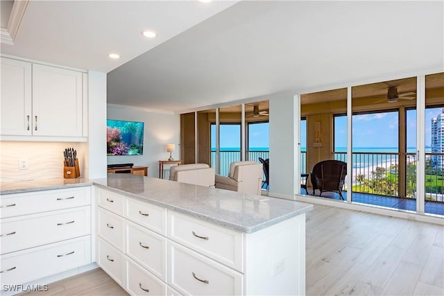 kitchen featuring open floor plan, light wood-style flooring, a peninsula, light stone countertops, and recessed lighting