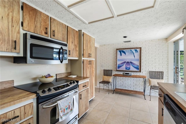 2209 SE 10th Ave, Cape Coral, FL 33990 - kitchen featuring brown cabinetry, a textured ceiling, appliances with stainless steel finishes, light tile patterned flooring, and brick wall