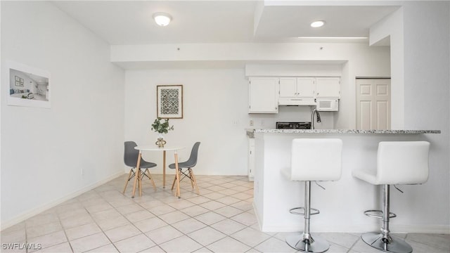 kitchen featuring white cabinets, under cabinet range hood, a kitchen bar, a peninsula, and white microwave