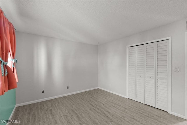 unfurnished bedroom featuring baseboards, wood finished floors, a textured ceiling, and a closet