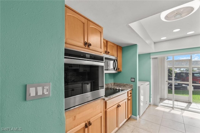 kitchen featuring black electric stovetop, stainless steel microwave, a textured wall, washer and dryer, and light tile patterned floors