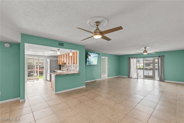 unfurnished living room featuring visible vents, a textured ceiling, ceiling fan, and a healthy amount of sunlight