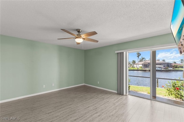 empty room with wood finished floors, a textured ceiling, a water view, and ceiling fan