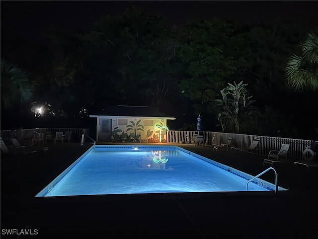 pool at night with an outdoor structure, a shed, a community pool, and fence