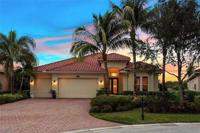 mediterranean / spanish home with a tiled roof, an attached garage, decorative driveway, and stucco siding