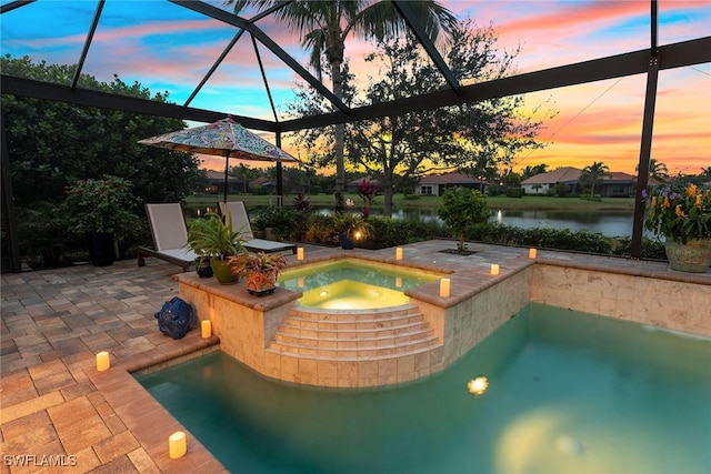 pool at dusk with a patio area, an in ground hot tub, glass enclosure, and a water view