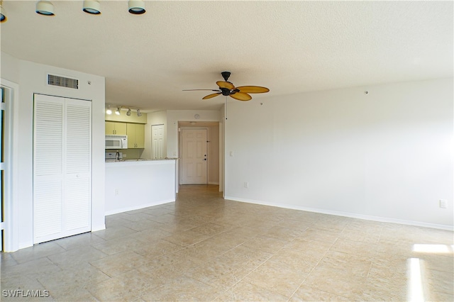 unfurnished living room featuring ceiling fan, rail lighting, a textured ceiling, visible vents, and baseboards