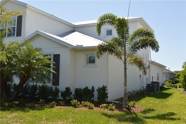 view of side of home with stucco siding, central air condition unit, a yard, and metal roof