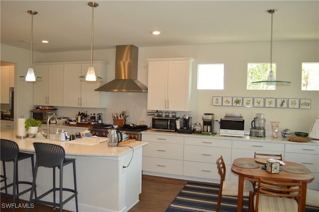 kitchen with white cabinets, dark wood-style floors, a breakfast bar, wall chimney exhaust hood, and range