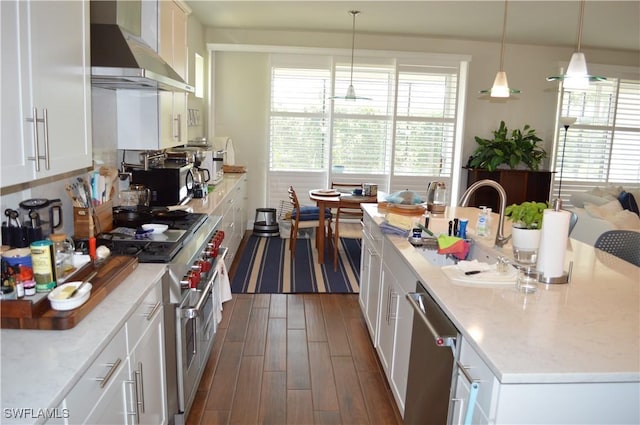 kitchen featuring stainless steel appliances, a healthy amount of sunlight, white cabinetry, and wall chimney range hood