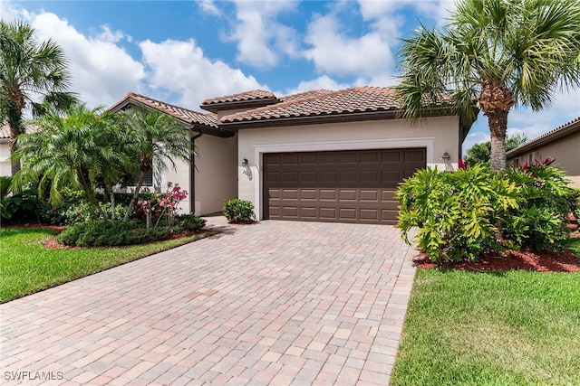 mediterranean / spanish house with a tiled roof, decorative driveway, a garage, stucco siding, and a front yard
