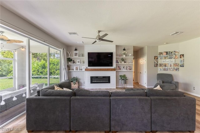 living room with a fireplace, a ceiling fan, light wood-style flooring, and baseboards