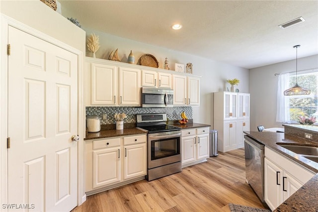 kitchen with stainless steel appliances, backsplash, decorative light fixtures, light wood-style flooring, and white cabinetry