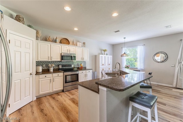 kitchen with stainless steel appliances, a sink, a kitchen breakfast bar, light wood finished floors, and recessed lighting