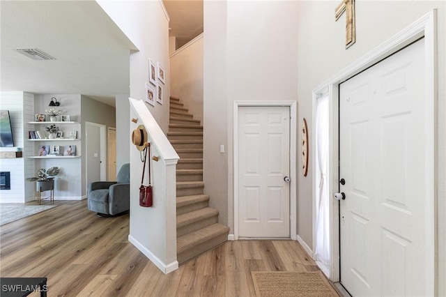 foyer with light wood-type flooring, stairs, a large fireplace, baseboards, and a high ceiling