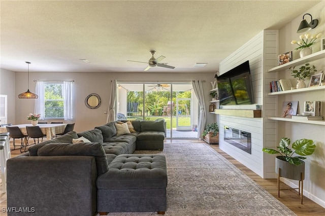 living area with ceiling fan, healthy amount of natural light, a large fireplace, wood finished floors, and a textured ceiling