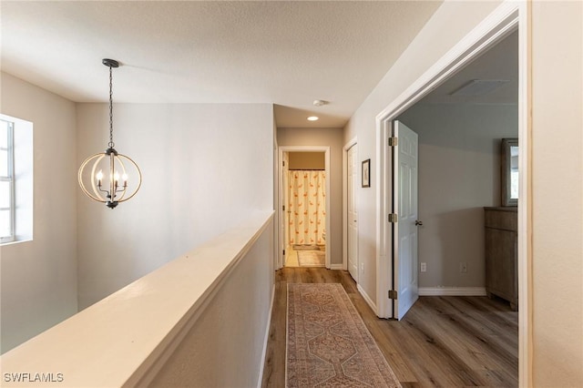 hall featuring wood finished floors, a chandelier, baseboards, and recessed lighting