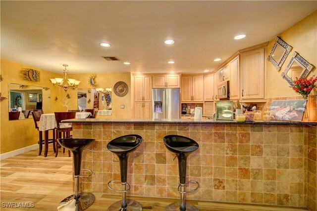 kitchen with visible vents, appliances with stainless steel finishes, stone countertops, light wood-style flooring, and a breakfast bar area