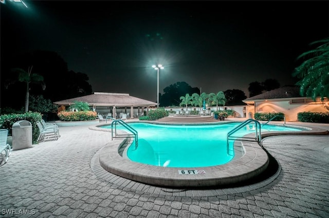 576 Retreat Dr Unit 101, Naples, FL 34110 - pool at night featuring an outbuilding, a patio area, an exterior structure, and a community pool