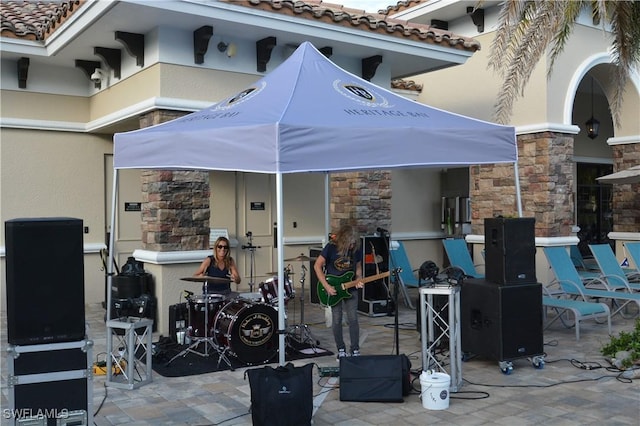 exterior space with a tile roof, stone siding, a patio, and stucco siding