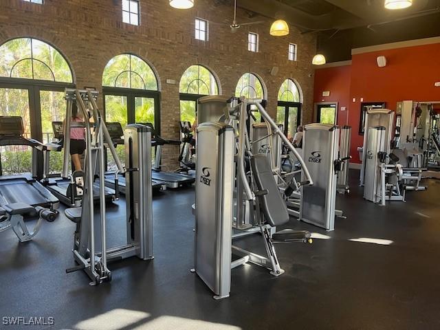 8945 Malibu St Unit 204, Naples, FL 34113 - exercise room featuring a healthy amount of sunlight, a high ceiling, and brick wall