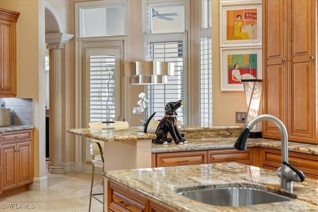550 21st Ave S, Naples, FL 34102 - kitchen featuring light stone countertops, brown cabinetry, decorative columns, and a sink