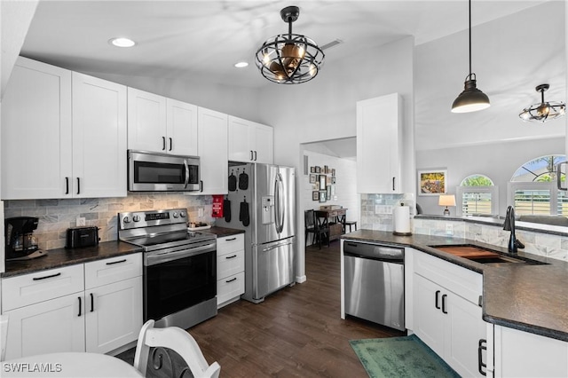 kitchen with a notable chandelier, a sink, appliances with stainless steel finishes, dark countertops, and dark wood finished floors