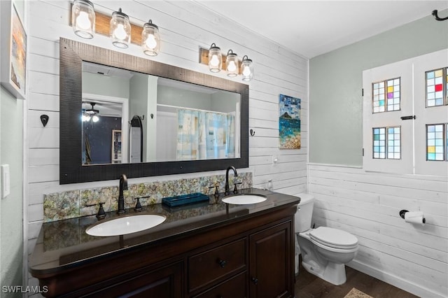 bathroom featuring toilet, double vanity, wood walls, and a sink