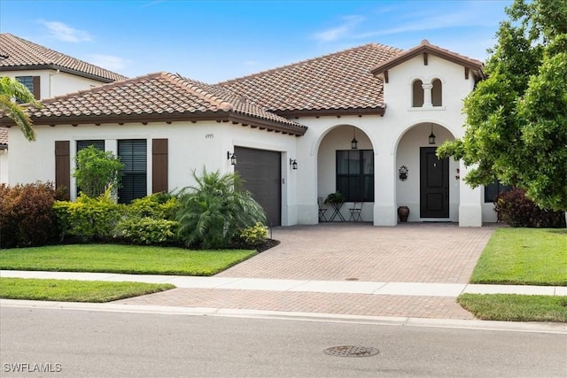 mediterranean / spanish house with a front yard, a tiled roof, a garage, stucco siding, and decorative driveway