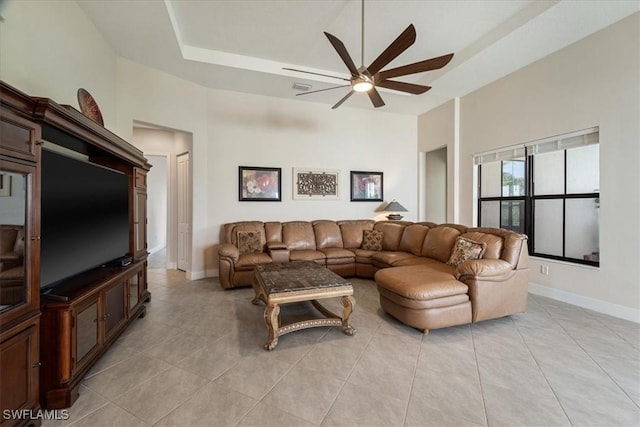 living area with a tray ceiling, light tile patterned floors, baseboards, and a ceiling fan