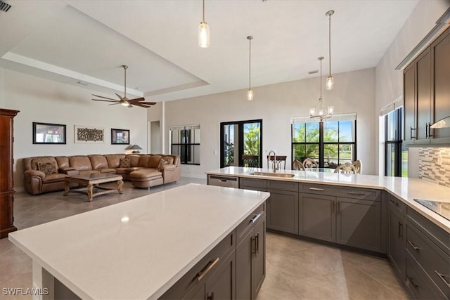 kitchen with open floor plan, a peninsula, light countertops, a tray ceiling, and a sink