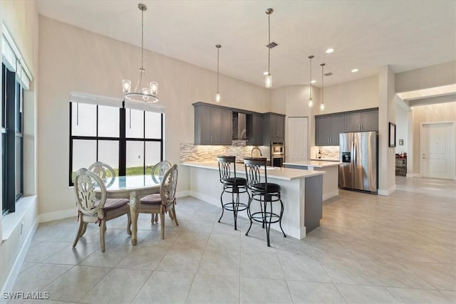 kitchen featuring wall chimney range hood, a peninsula, light countertops, backsplash, and appliances with stainless steel finishes