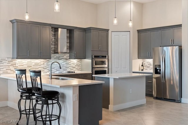 kitchen featuring a peninsula, wall chimney range hood, a center island, a sink, and stainless steel appliances